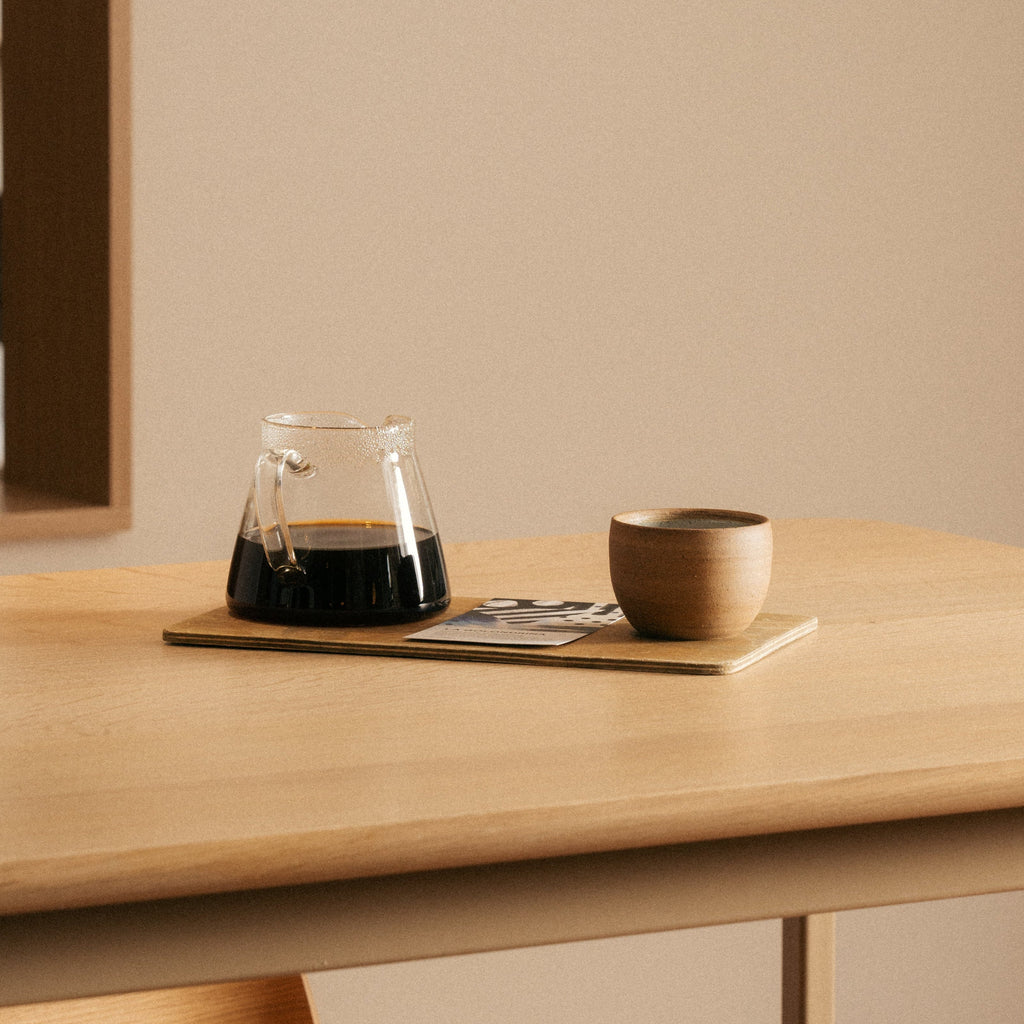 Glass coffee carafe and wooden mug on a wooden table with a neutral background