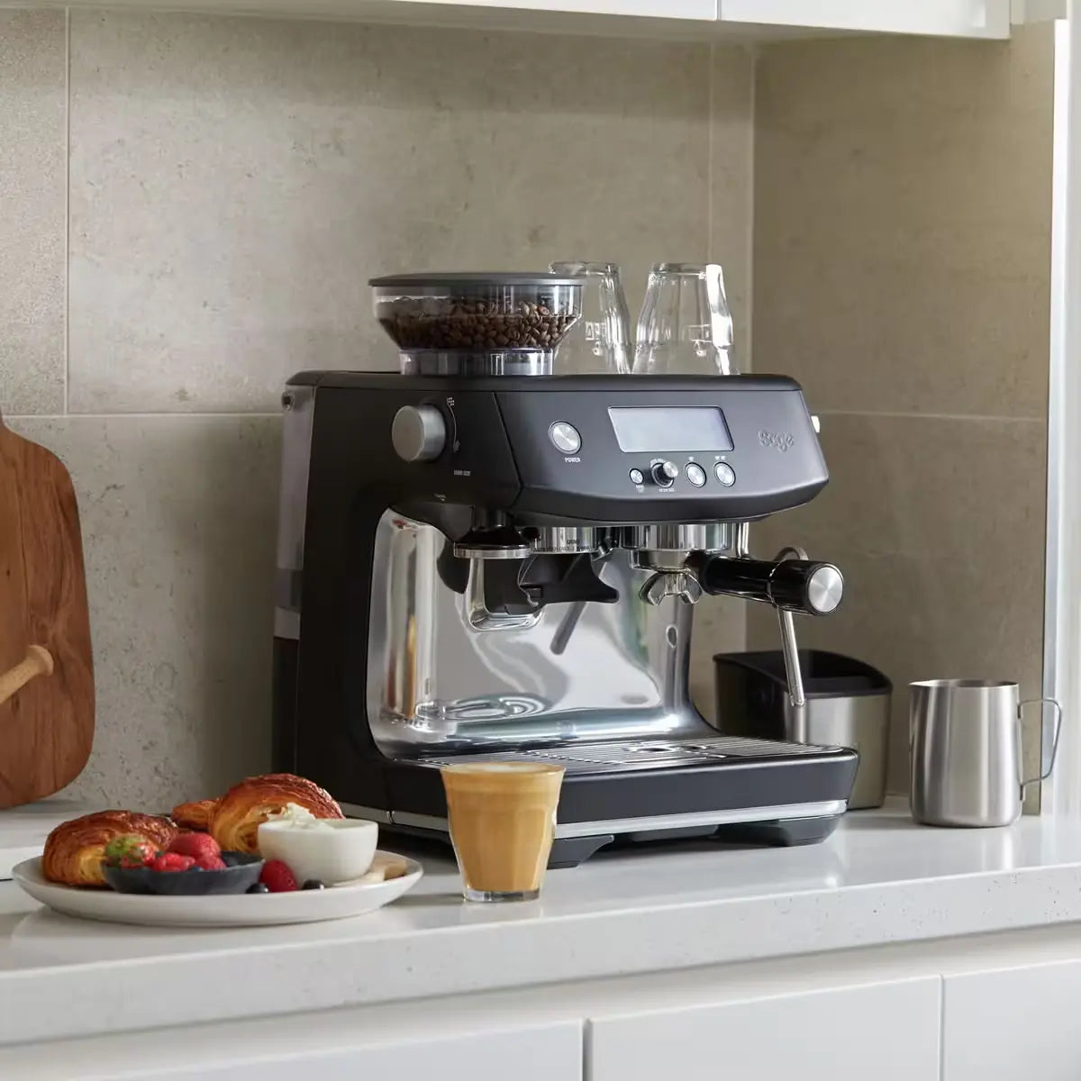 A black Sage Barista Pro espresso machine on kitchen counter displaying its built-in grinder, LCD display, and steam wand, designed for home coffee brewing